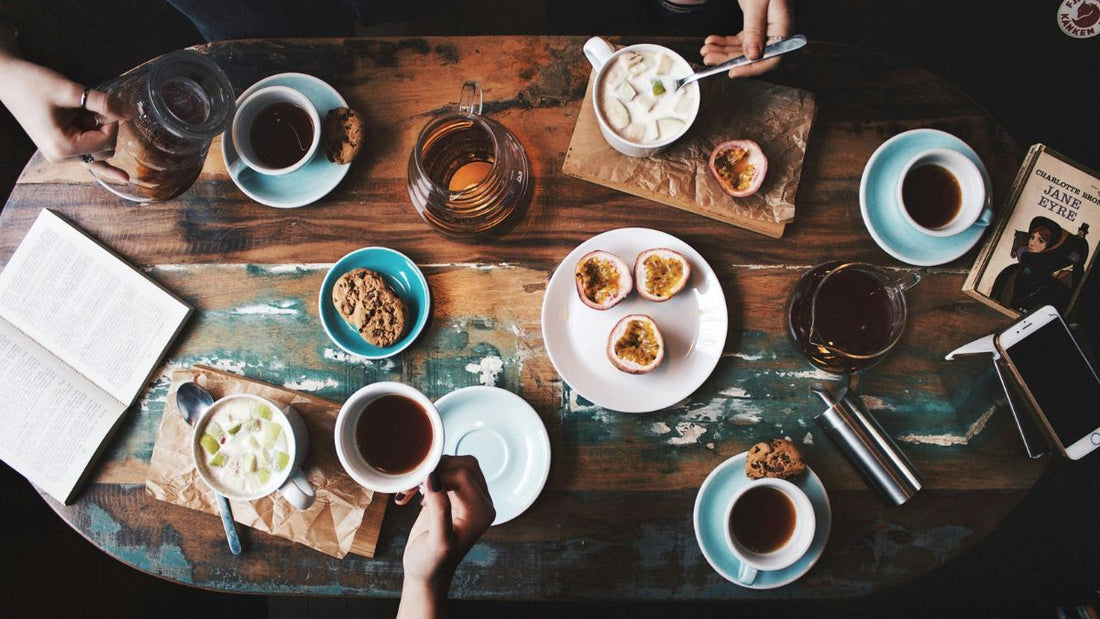 Drewniany stół z filiżankami kawy i talerzykami z drobnymi przekąskami, symbolizujący spotkanie przyjaciółek i zdrowe podejście do jedzenia bez liczenia kalorii w Shape Your Plate.